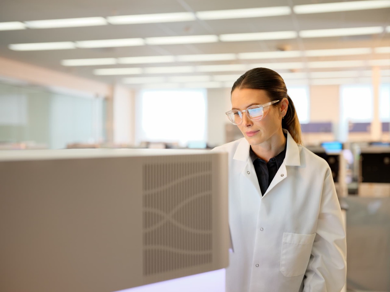Front view of female scientist looking at the touch screen on a NextSeq 1000/2000 in a dry lab.